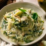 Lemon ricotta zucchini noodles topped with Parmesan, fresh basil, and toasted pine nuts in a shallow bowl.