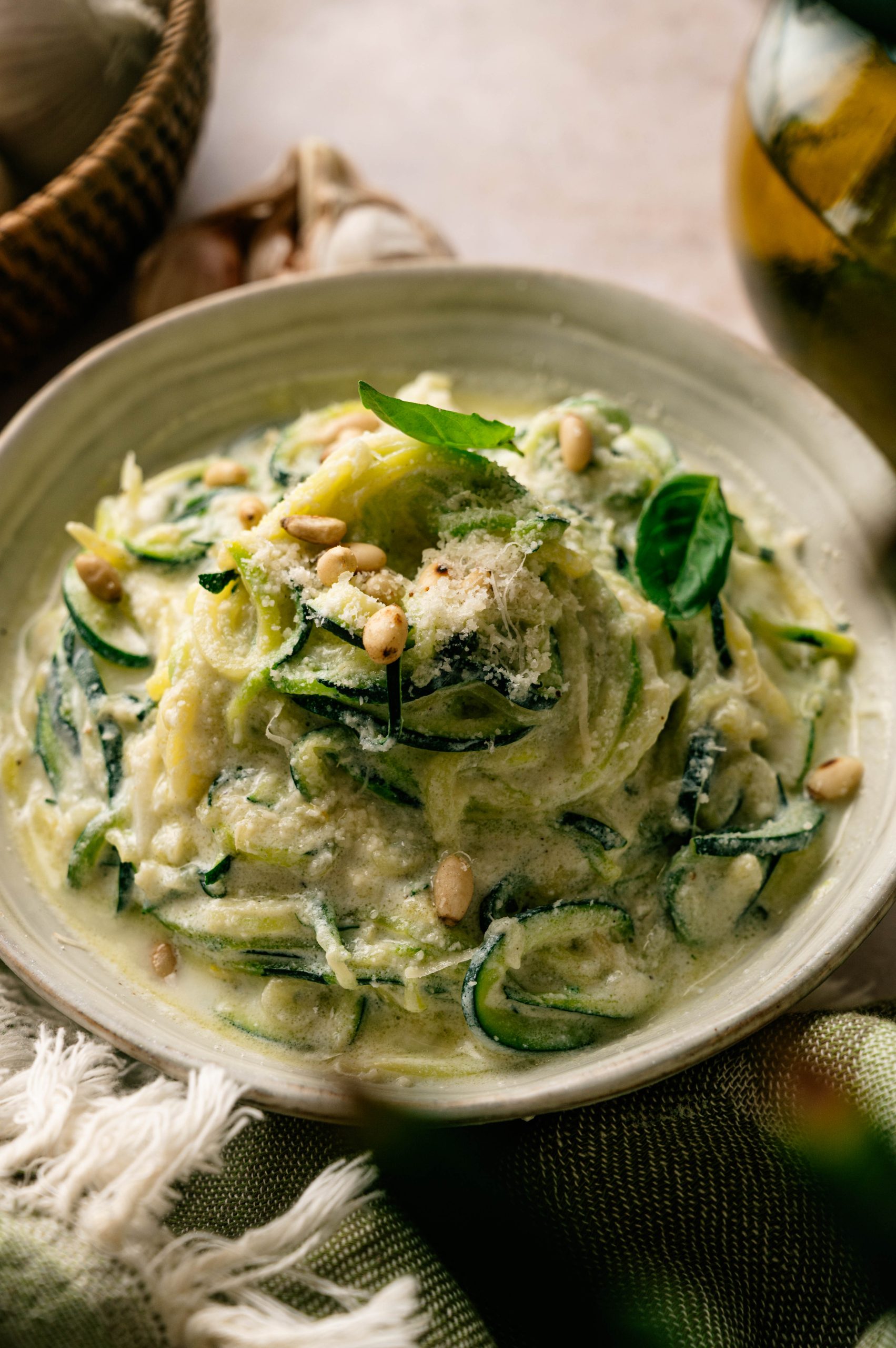 Lemon ricotta zucchini noodles topped with Parmesan, fresh basil, and toasted pine nuts in a shallow bowl.