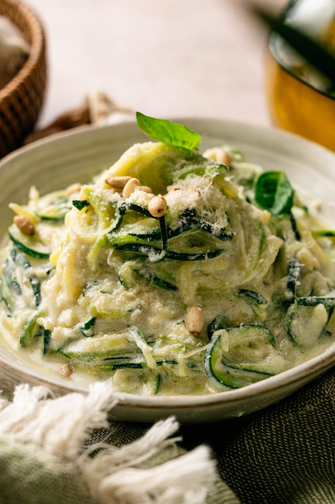 Close-up of lemon ricotta zucchini noodles coated in creamy sauce and topped with Parmesan, basil, and pine nuts.