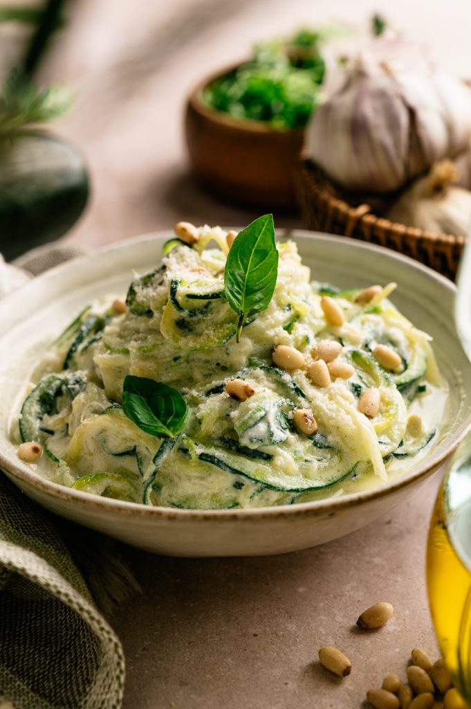 Lemon ricotta zucchini noodles topped with Parmesan, fresh basil, and toasted pine nuts in a shallow bowl.
