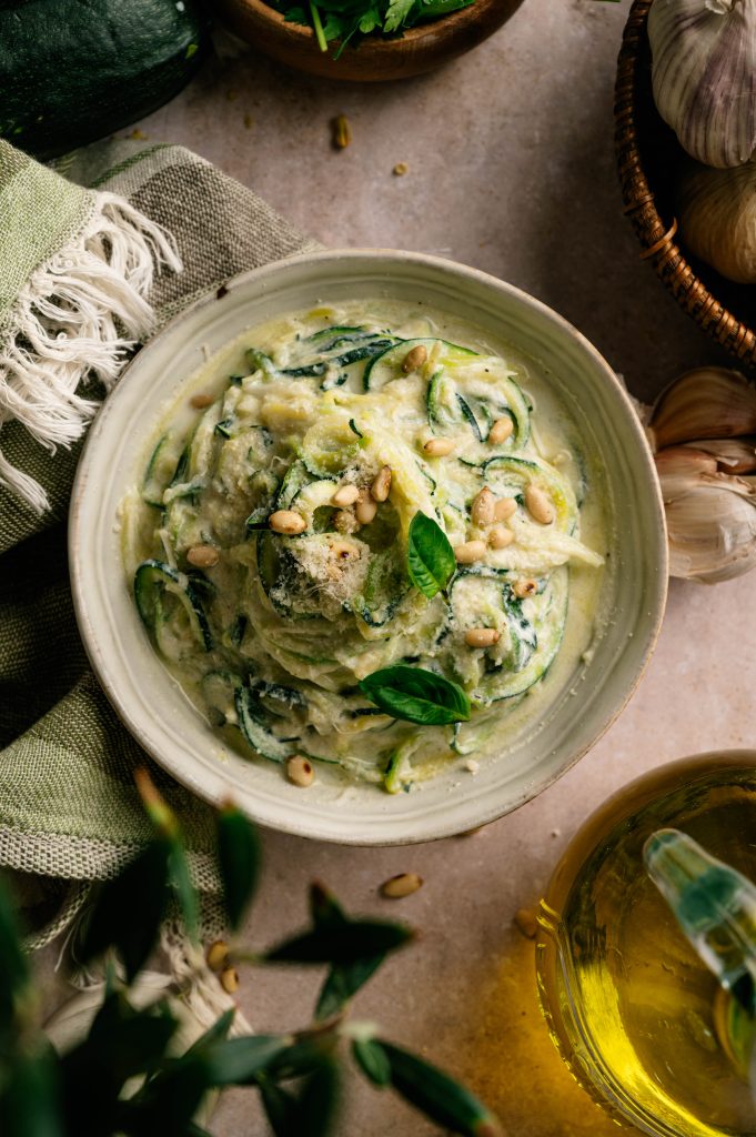Overhead view of creamy lemon ricotta zucchini noodles finished with basil, Parmesan, and pine nuts.