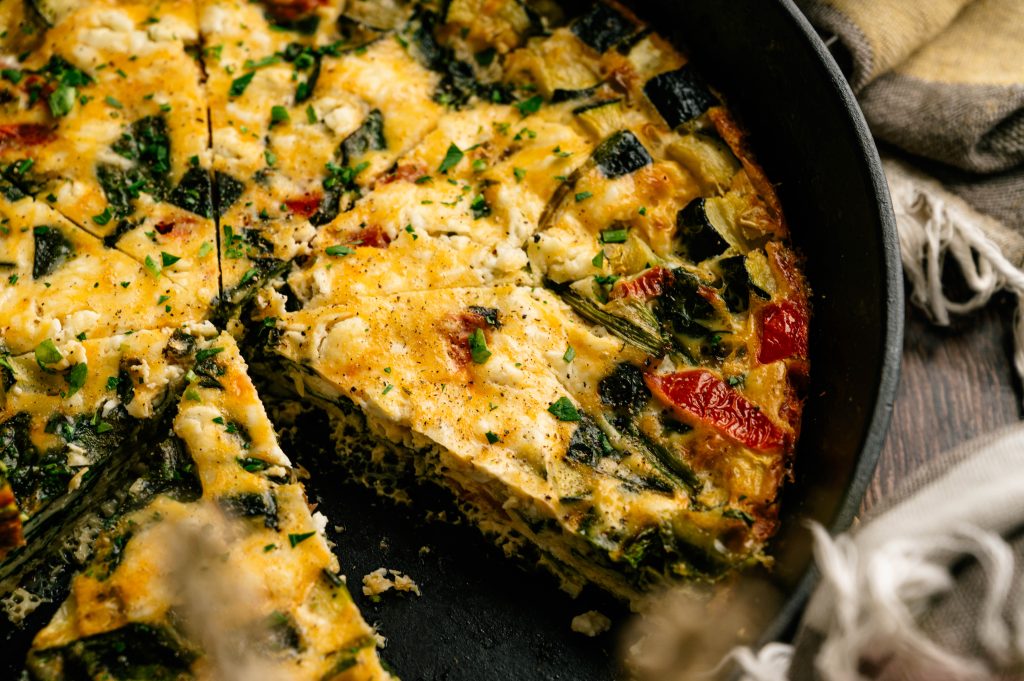 Garden zucchini frittata cut into wedges in a cast iron skillet with a golden top and tender vegetable filling.