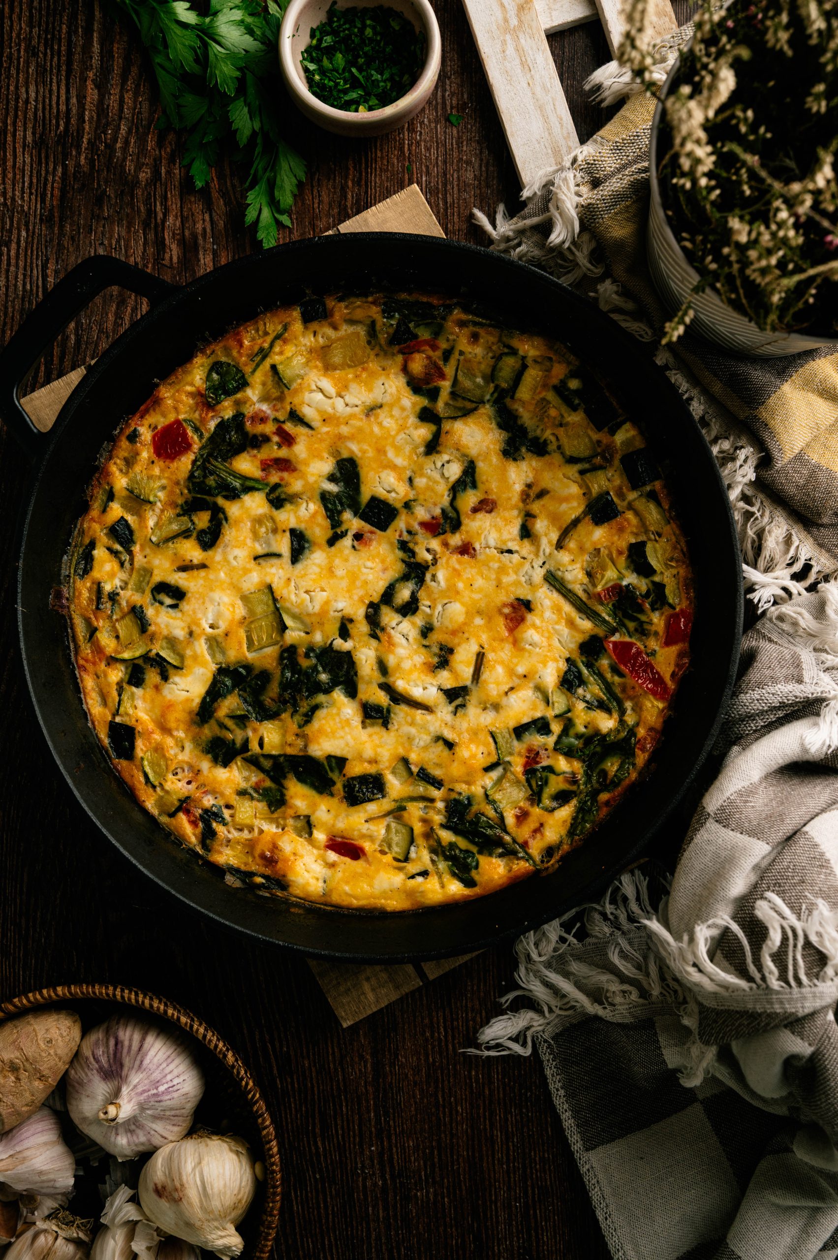 Garden zucchini frittata in a cast iron skillet with tomatoes, spinach, and cheese.