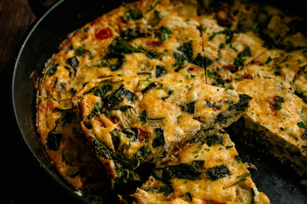 Close-up of sliced garden zucchini frittata with spinach, tomatoes, and cheese in a cast iron skillet.