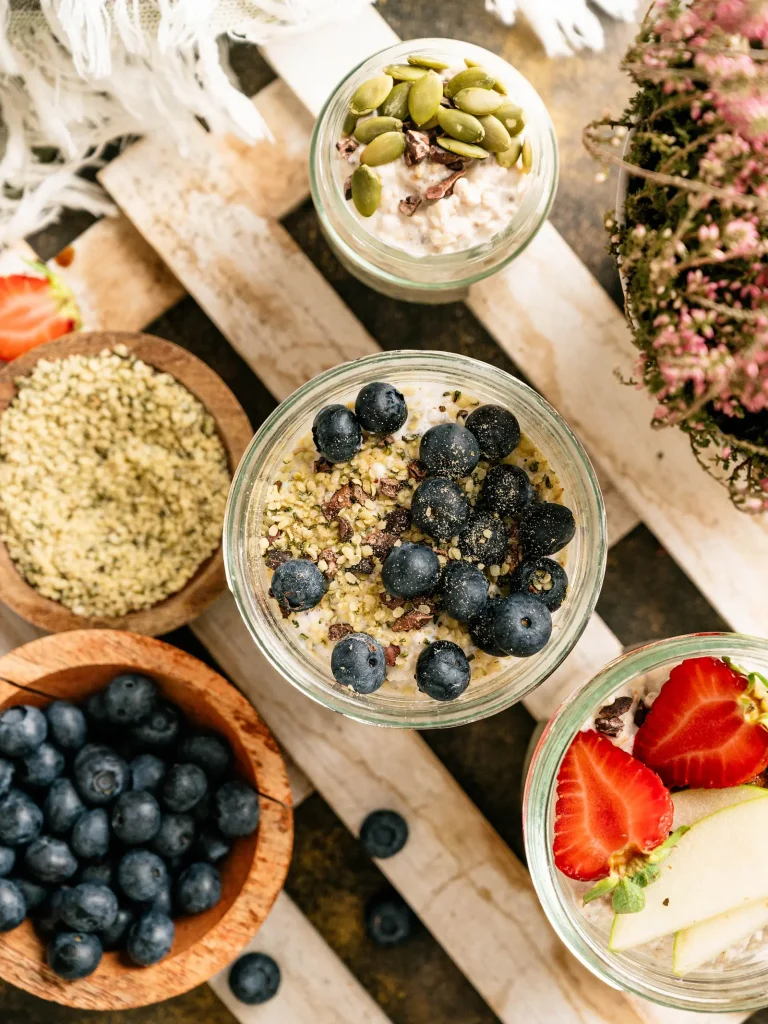 Blueberry overnight oats with kefir in glass jars surrounded by fruit and seeds