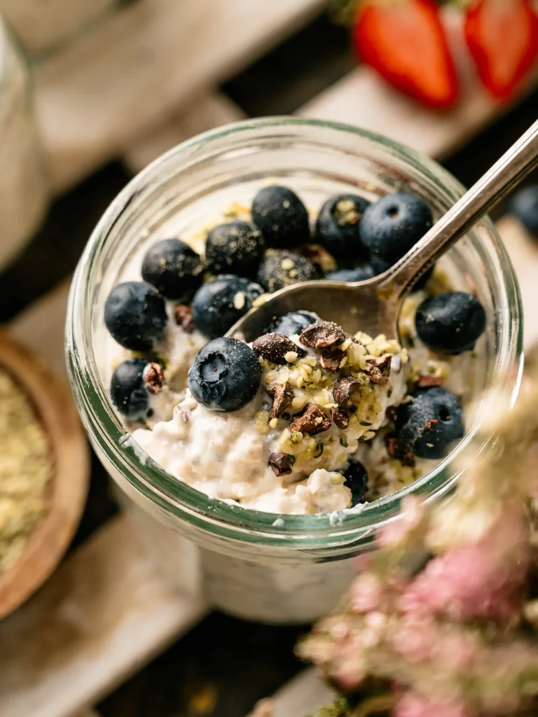 Spoon lifting creamy overnight oats with blueberries and seeds from a glass jar
