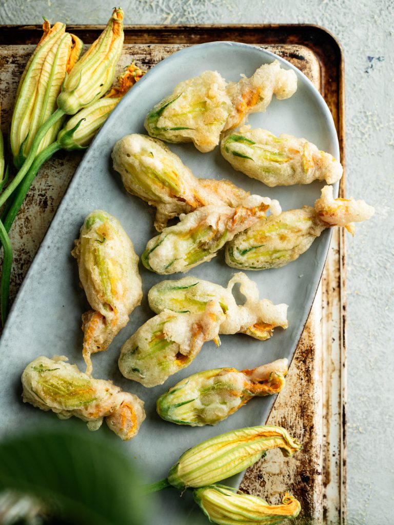Overhead view of fried stuffed zucchini blossoms on a gray platter with fresh flowers