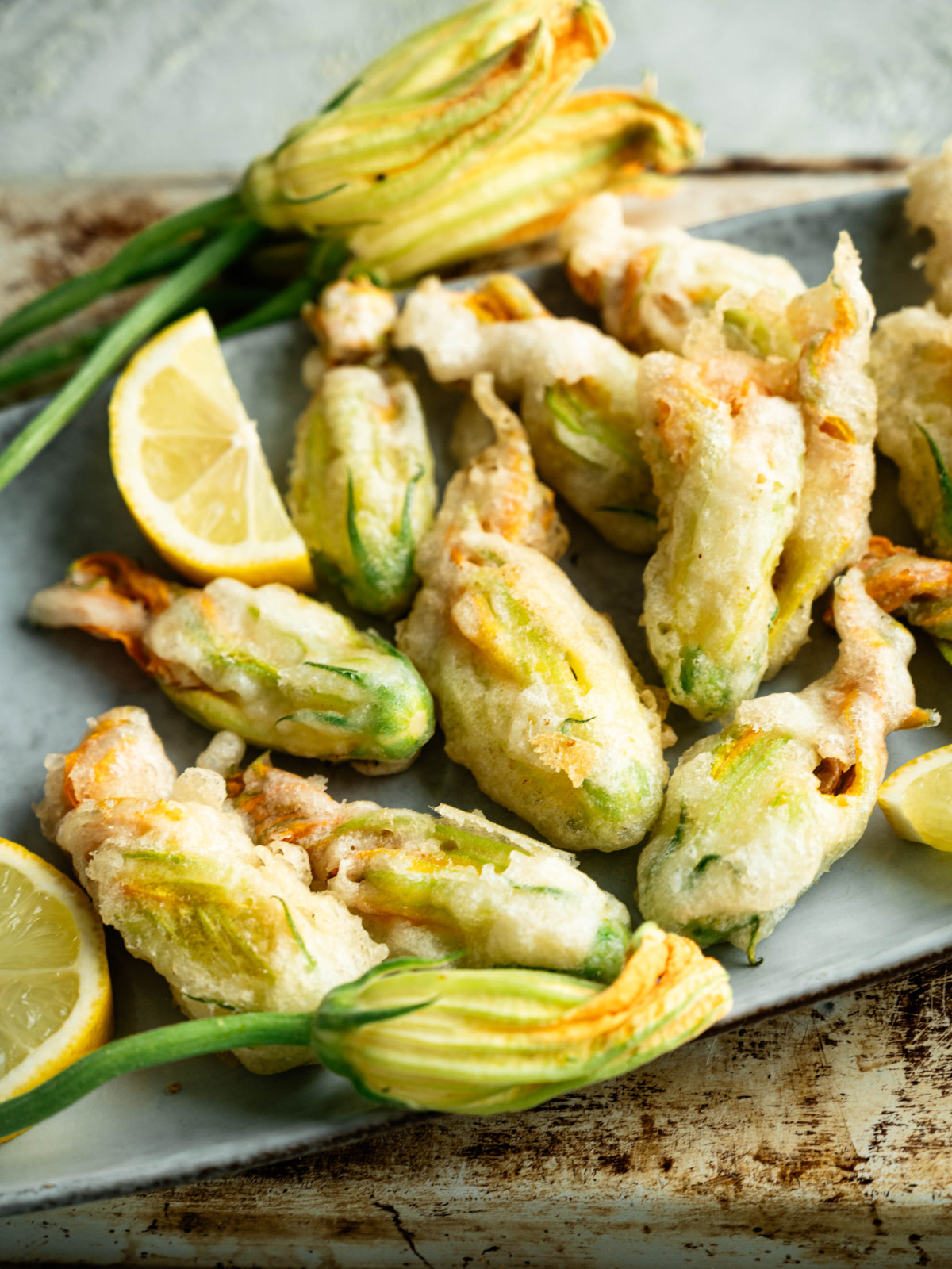 Close-up of crisp fried zucchini blossoms with lemon wedges and fresh blossoms