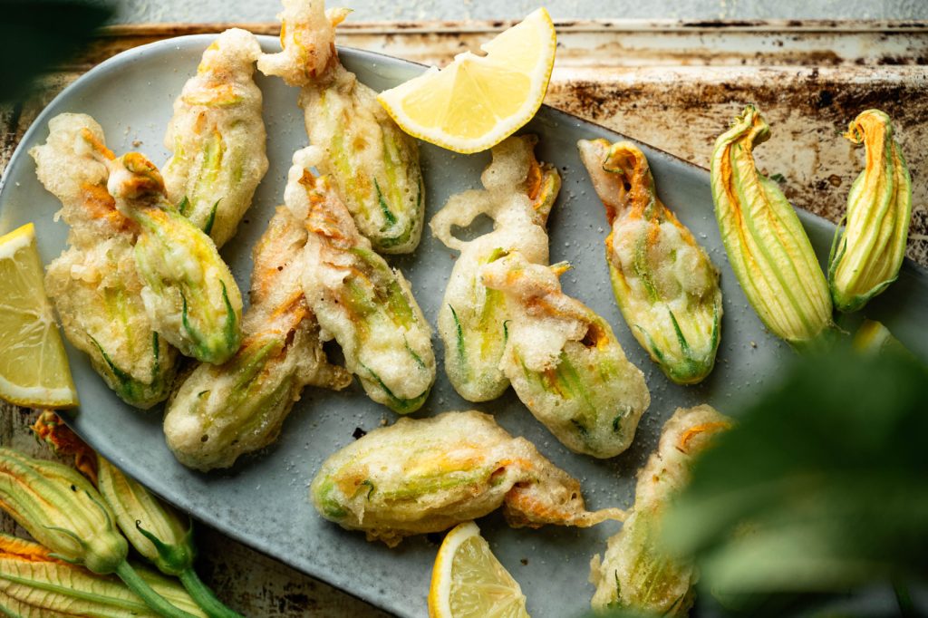 Overhead platter of crisp fried zucchini blossoms with lemon and fresh flowers