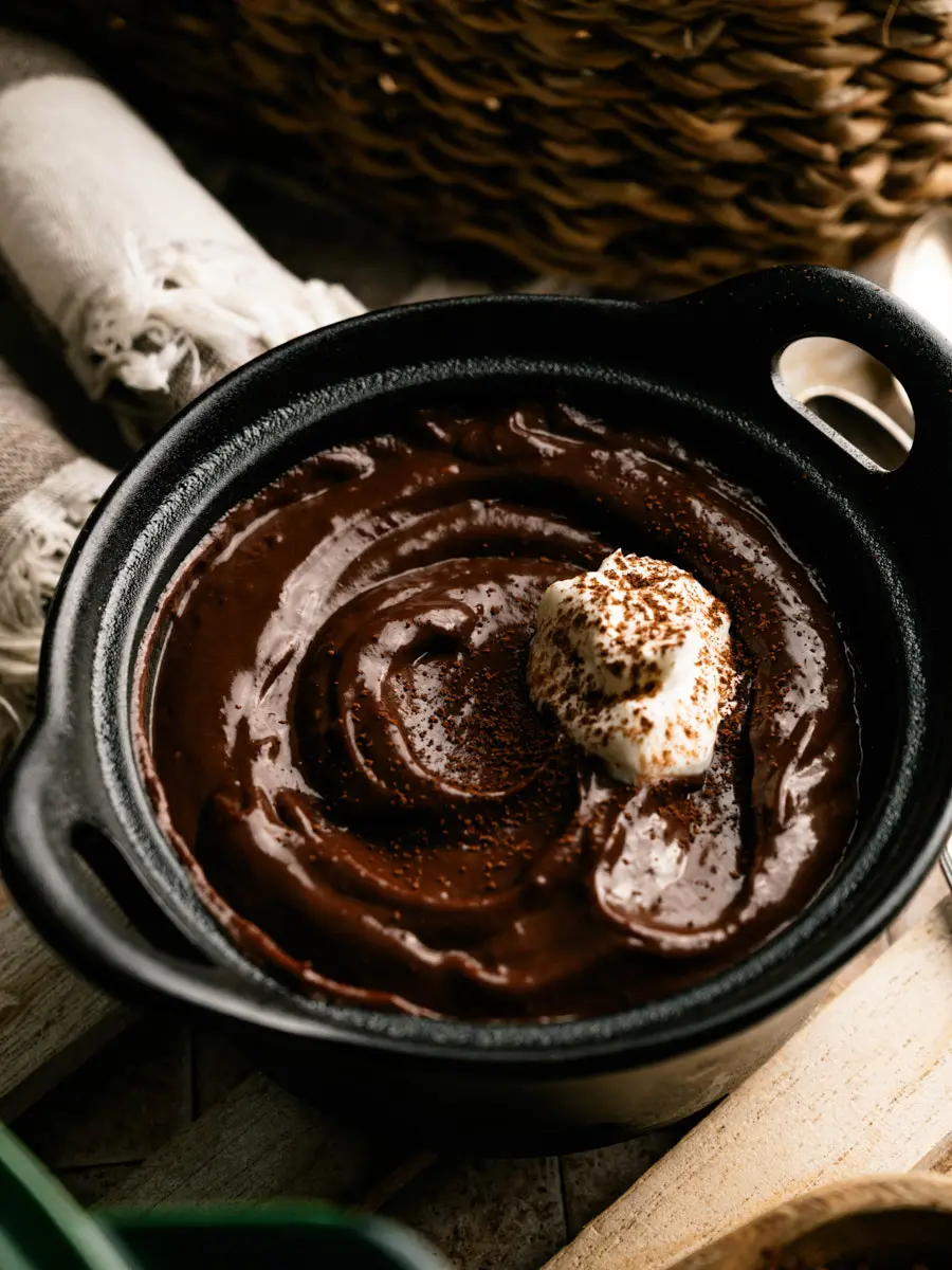 Chocolate pudding topped with whipped cream and cocoa in a black bowl