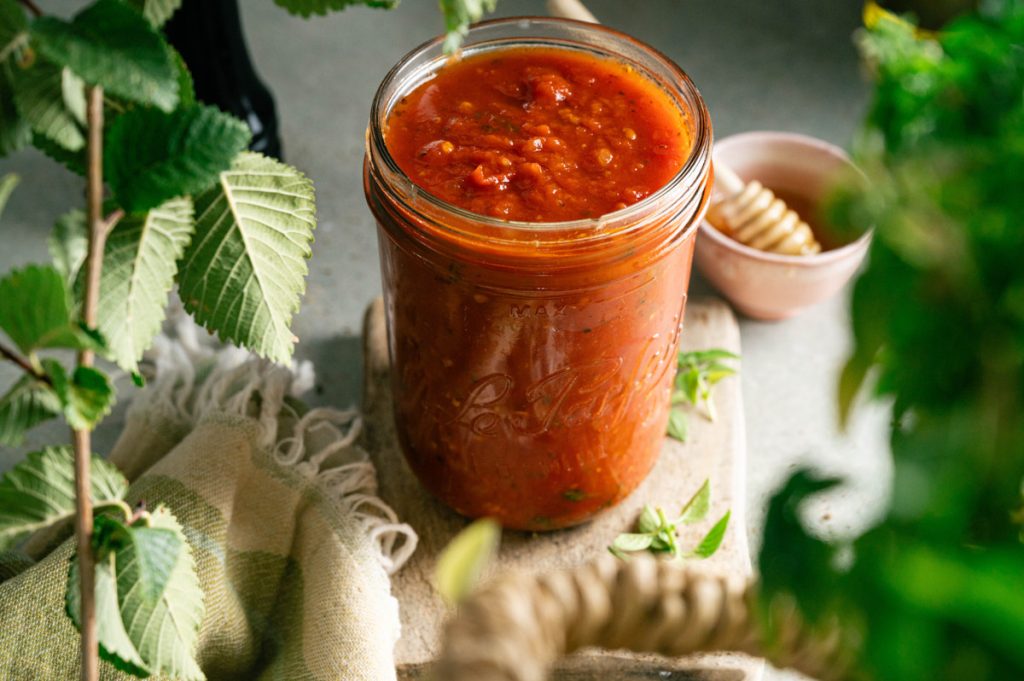 Jar of homemade marinara sauce styled with fresh basil and kitchen linens