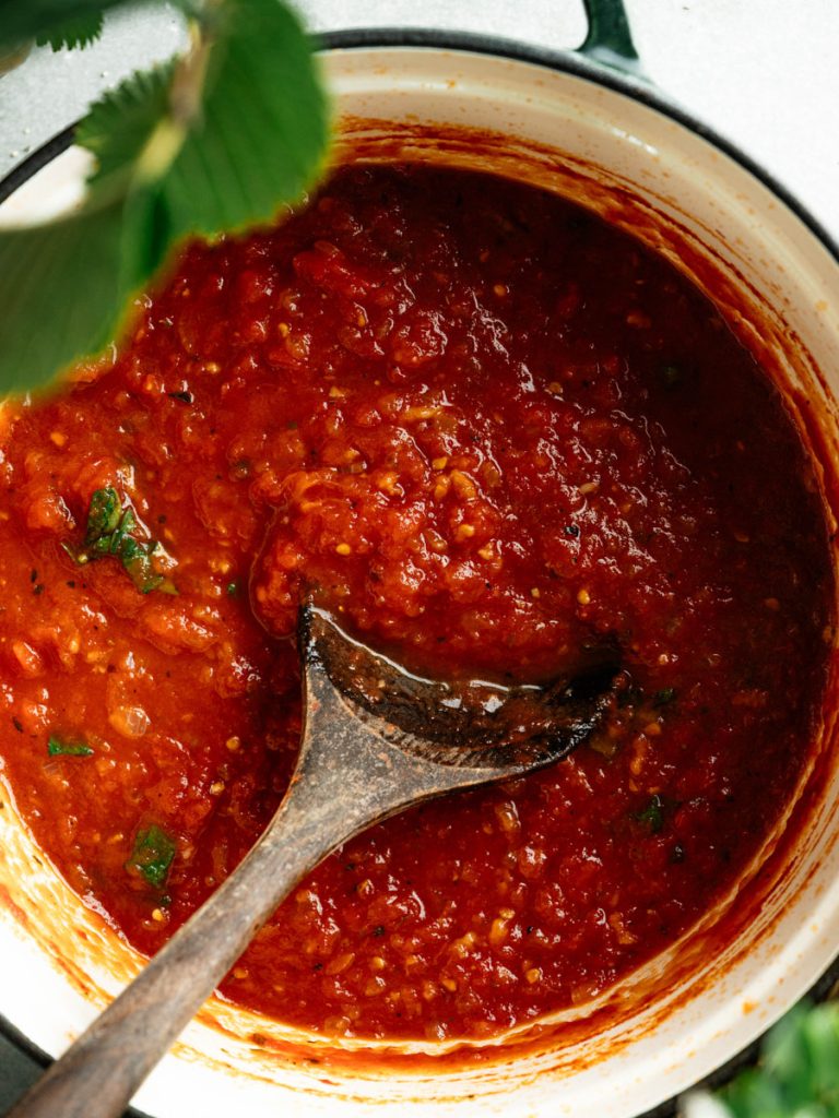 Rustic homemade marinara sauce with a metal ladle and fresh basil