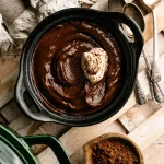 Silky chocolate pudding topped with whipped cream and cocoa in a dark bowl