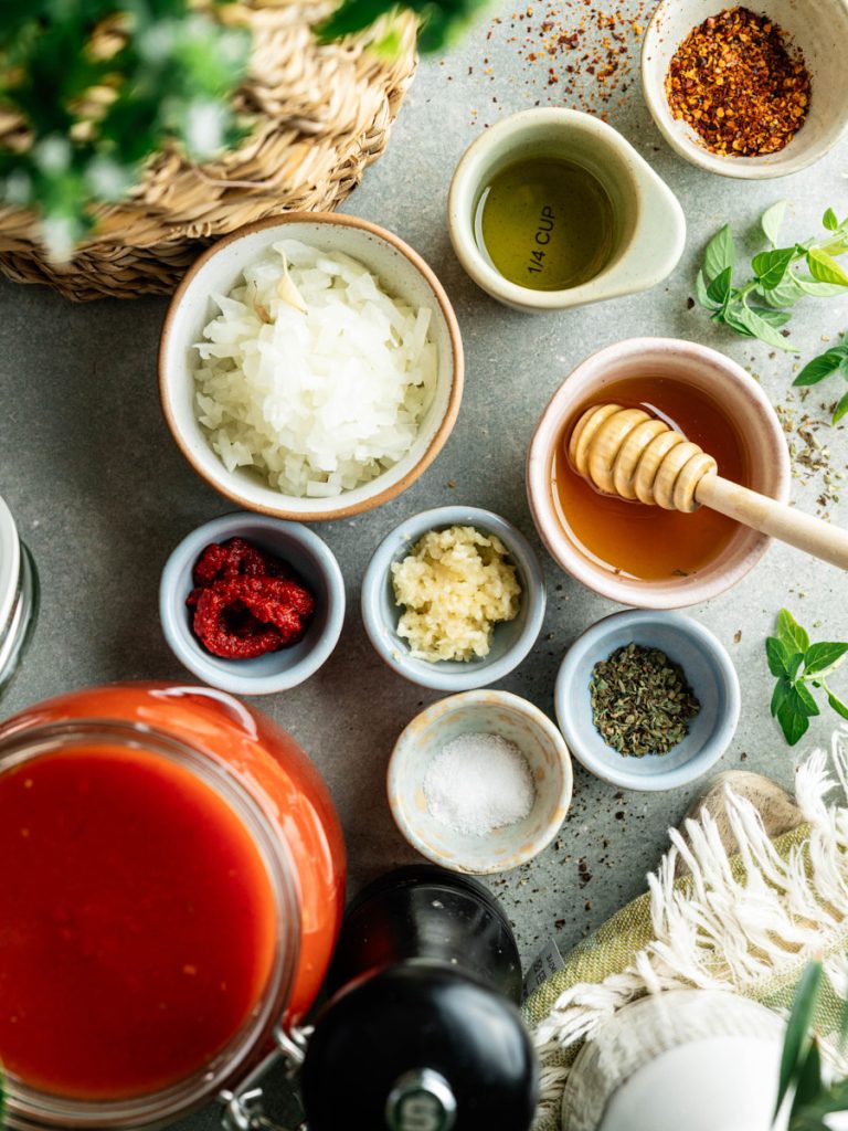 Ingredients for simple homemade marinara sauce arranged around a pot of tomatoes