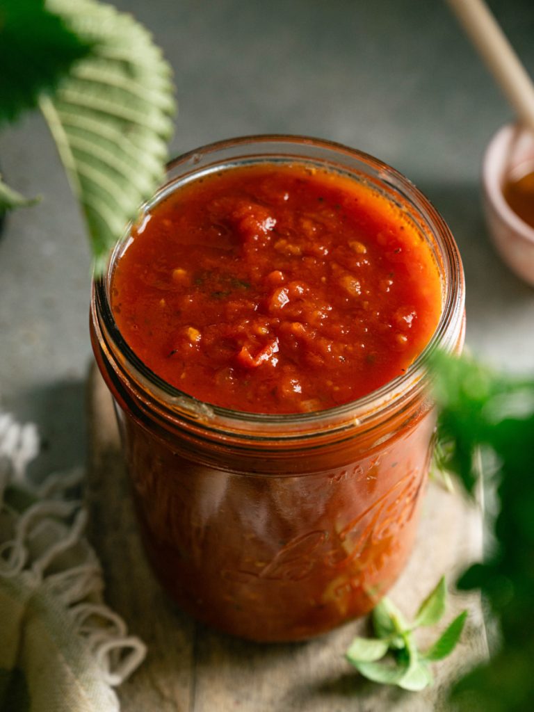 Glass jar filled with simple homemade marinara sauce beside fresh basil