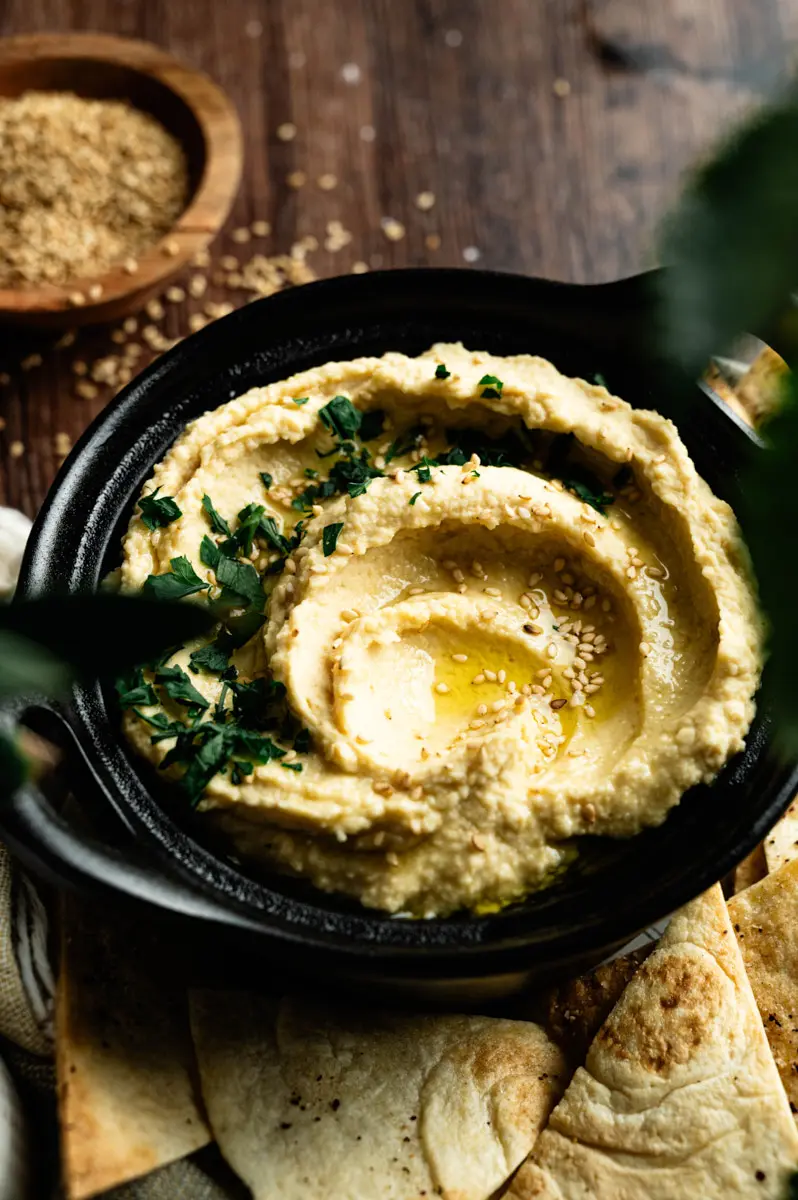 Smooth homemade hummus with olive oil and herbs in a black serving bowl