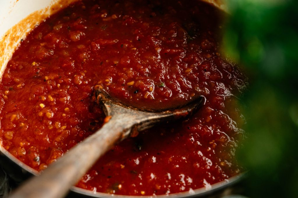 Wooden spoon stirring rustic homemade marinara sauce in a pot