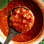 Ladle filled with thick homemade marinara sauce over a pot of tomato sauce