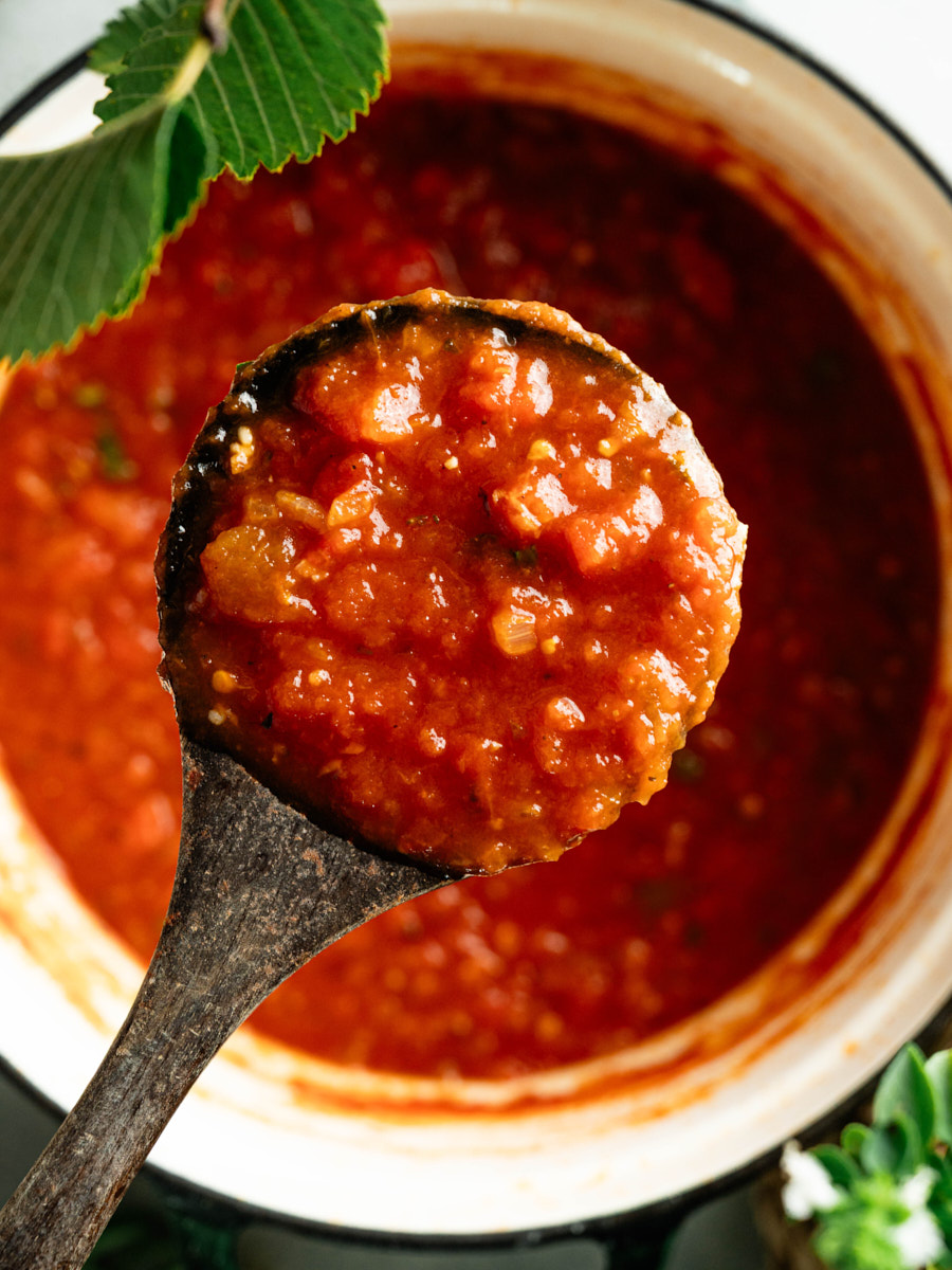 Ladle filled with thick homemade marinara sauce over a pot of tomato sauce