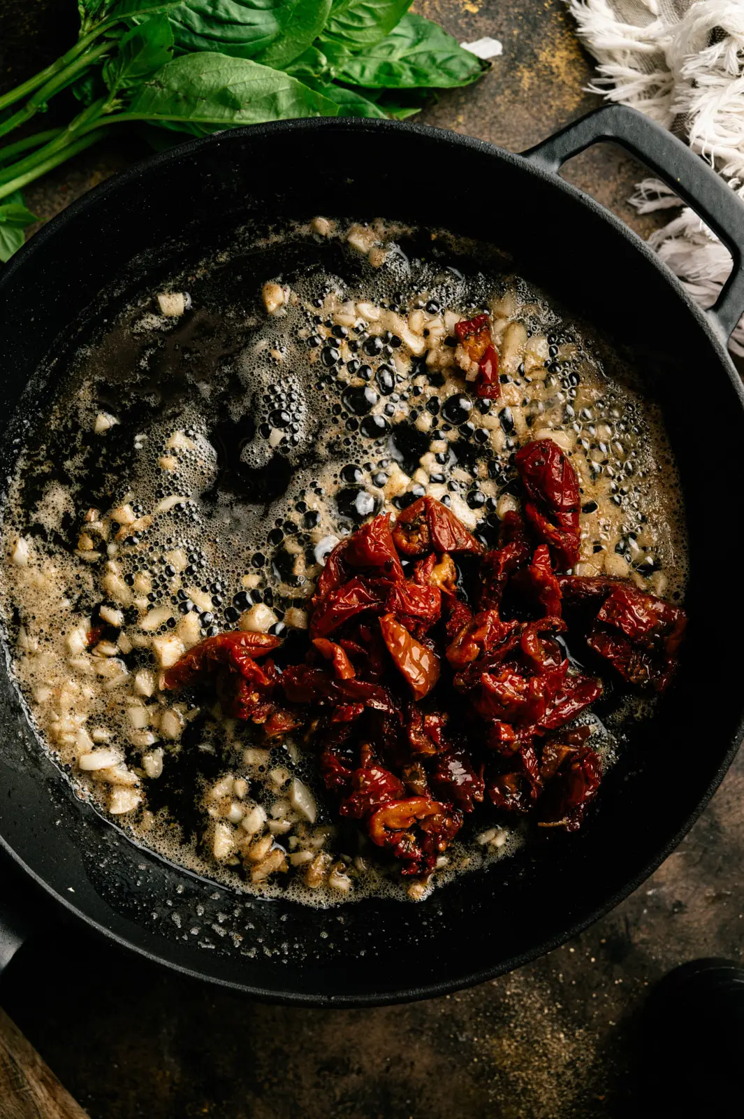 Chopped garlic and sun-dried tomatoes in bubbling butter in a black cast-iron skillet.